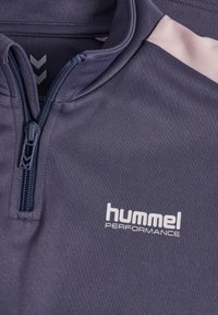 Marineblauw sportief bovenstuk met rits en roze accenten op de schouders, gemaakt van gestructureerde stof. Voorzien van het "hummel PERFORMANCE"-logo in het wit ter hoogte van de borst.