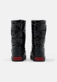 Stivali neri impermeabili con una parte superiore imbottita lucida, progettati per il calore, con un logo Sorel rosso sul tallone e una suola nera solida.