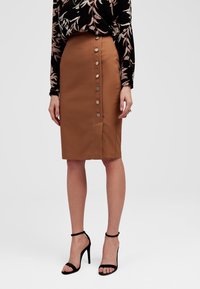Brąskowa spódnica o kroju ołówkowym z guzikami z przodu, wykonana z gładkiego materiału. W połączeniu z czarnymi szpilkami na kostkę. Kwiatowa bluzka z długim rękawem.