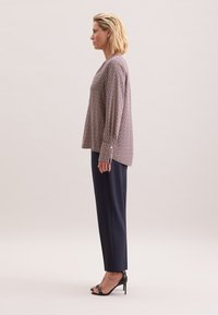 Blusa a maniche lunghe, stampata e realizzata in un tessuto morbido, con scollatura tonda e polsini con bottoni, abbinata a pantaloni sartoriali blu navy e tacchi neri con cinturino.