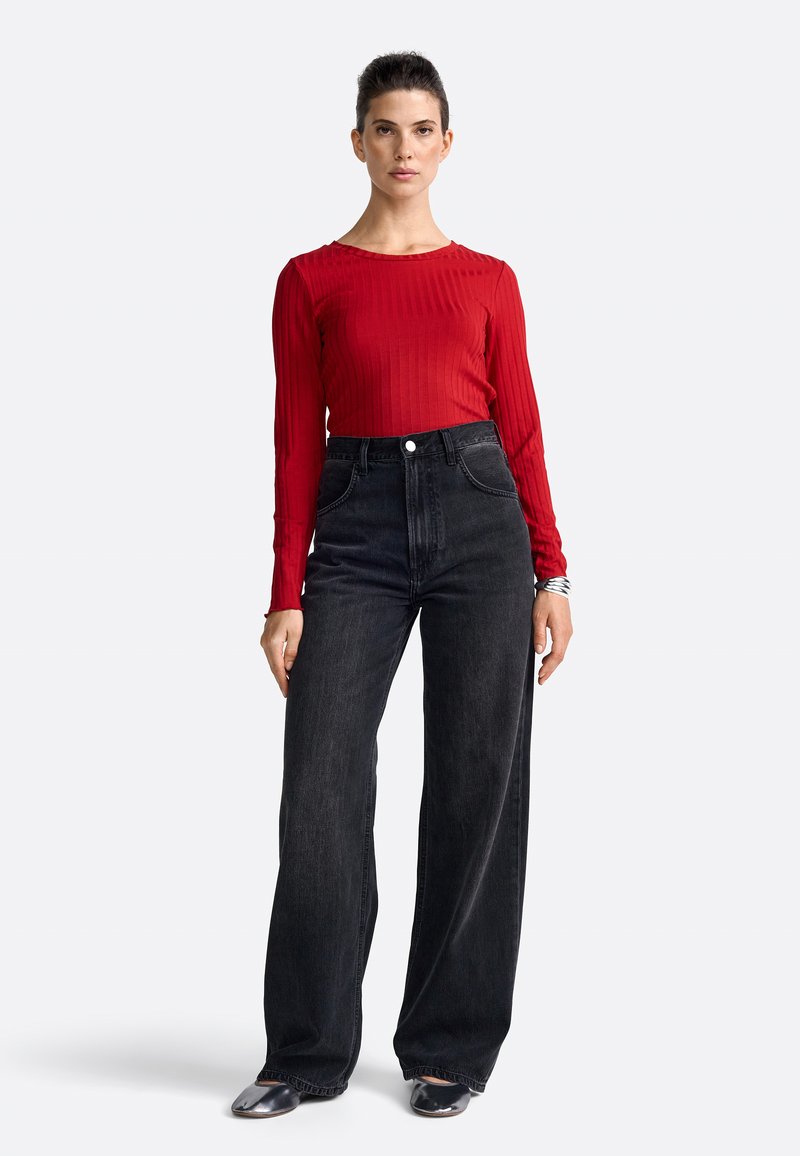 Rød ribbet langærmet top parret med højtaljede, sort brede jeans. Inkluderer en knaplukning og en glat, blød tekstur.