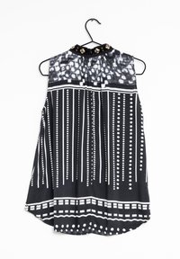 Blusa sin mangas en blanco y negro con patrones verticales y horizontales, adornada con tachuelas doradas en el escote y con un dobladillo curvado.