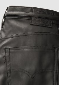 Czarne skórzane spodnie z dopasowanym krojem, wyjątkowymi wzorami przeszyć oraz emblematyczną skórzaną naszywką z logo na tylnym pasie.