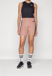 Czarny, bezrękawnik typu crop top, różowe szorty z wysokim stanem i czarnymi bocznymi paskami oraz czarne buty sportowe z białymi skarpetkami w paski.