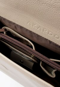 Interno di una borsa a mano in pelle beige con fodera in tessuto marrone, dotata di una tasca con zip e scomparti per l'organizzazione. Un logo è impressa all'interno.