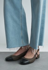 Brune mønstrede slingback-sko med en sort tåkappe, sat mod lyseblå slidte jeans. Subtile hardware-detaljer tilføjer nuance.
