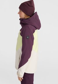 Damen-Skijacke mit einem Farbblockdesign in Lila, Gelb und Creme. Hergestellt aus einem wasserdichten Material mit hohem Kragen und verstellbarer Kapuze.