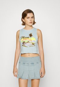 Top cropped azul claro com uma graphic de Miami que apresenta palmeiras e um surfista. Combinado com uma saia mini plissada de denim claro.