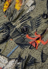 Látka s květinovým vzorem v zelených tónech s žlutými a červenými akcenty. Obsahuje černé knoflíky a texturované záhyby. Lehký materiál.