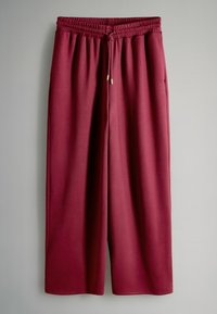 Bordo spalvos plataus kirpimo sportinės kelnės iš minkštos medžiagos, su elastinga juosmens juosta su raišteliais ir šoninėmis kišenėmis.