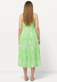 Zelené maxi šaty s tierovým střihem a tenkými ramínky. Materiál má bílý abstraktní vzor, měkkou texturu a uvolněný střih.