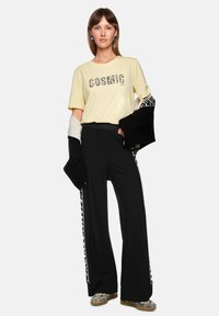 Yellow t-shirt with "COSMIC LOVE" text, black wide-leg pants with side stripes, oversized sleeves, and zebra print shoes.