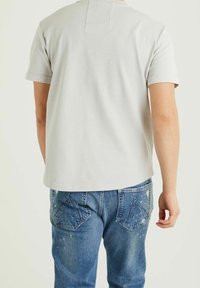 Jasnoszara koszulka z krótkim rękawem z teksturowanej tkaniny, z okrągłym dekoltem i detalem szwu z tyłu, w połączeniu z niebieskimi, zniszczonymi dżinsami.