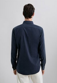Camisa abotonada de color azul oscuro con una textura suave, vista trasera que muestra un cuello clásico y mangas largas con puños abotonados.