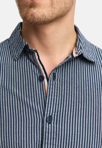 Camisa a rayas con líneas verticales en navy oscuro y gris claro, con cierre de botones y un detalle de cuello interior en contraste.