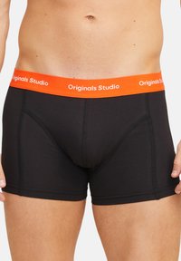 Boxer-briefs noirs avec une taille élastique orange portant l'inscription "Originals Studio", présentant un design ajusté et une texture douce.