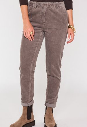 Grijze corduroy broek met een taps toelopende pasvorm, elastische tailleband en opgerolde mouwen. Gecombineerd met beige enkellaarzen en gouden accessoires.