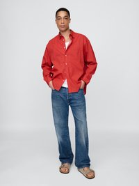 Röd rutmönstrad skjorta med långa ärmar, öppen krage, kombinerad med blå löst sittande jeans och grå sandaler. Minimalistisk design utan synliga mönster.