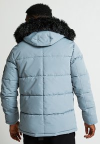 Šviesiai mėlynas pūkinis švarkas su nuimamu juodu kailiniu apdangalu. Jame yra horizontali siuvimo linija ir šiek tiek tekstūruotas paviršius.