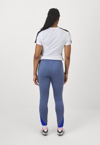 Sportoutfit met een witte gestructureerde korte mouw top met zwarte accenten en blauwe legging, die het gestroomlijnde ontwerp en de elastische tailleband benadrukt.