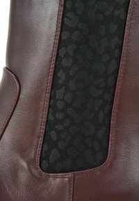 Bordeauxrode leren enkellaars met een gestructureerd zwart elastisch paneel met een subtiel luipaarddessin en contrasterende stikseldetails.