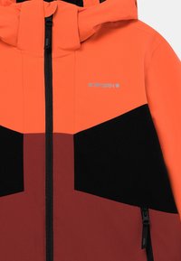 Giacca bloccata nei colori arancione e marrone scuro, realizzata in tessuto liscio. Presenta una chiusura a zip sul davanti, cappuccio e dettaglio del logo in grigio sulla parte superiore sinistra.