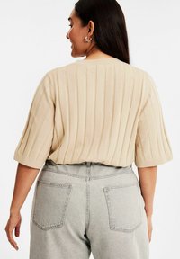Beige ribbat tröja med korta, vida ärmar, bärs med grå jeans med hög midja som har bakfickor och rak bendesign.