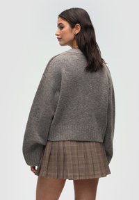 Šedý pletený svetr s volnými rameny a žebrovaným lemem, který je spárován s plisovanou kostkovanou sukní v béžových, hnědých a černých tónech.