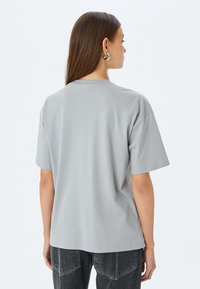 Camiseta de algodón suave de color gris claro, de manga corta y corte relajado, con escote redondo. Vista trasera mostrada.