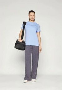 Gaiši zils t-krekls ar "Champion" logotipu, kombinēts ar vaļīgām pelēkām biksēm un melnu plecu somu. Gluda auduma, ar ikdienišķu piegriezumu.