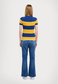 Knitted short-sleeve sweater with blue and yellow horizontal stripes, featuring a textured cable design and a white ribbed collar. Paired with blue flared jeans.