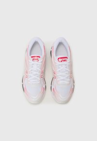 White athletic shoes with pink accents, mesh upper, laces, and textured sole. Features logo on tongue and contrasting design lines.
