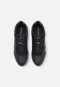 Black sneakers featuring a mix of smooth and textured materials, subtle logo pattern, laces, and a rubber sole. No visible branding on the sides.