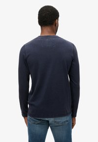 Navy long-sleeve shirt with a round neckline and a rectangular patch on the back, made of soft fabric, paired with blue denim jeans.