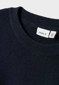Pull en maille bleu marine avec une texture côtelée et un col rond. L'étiquette intérieure indique la marque "name it" et les informations de taille.