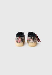 Fekete és piros houndstooth mintázatú cipők, puha tapintással, fekete bőr kiegészítőkkel és világos színű, texturált gumitalppal.