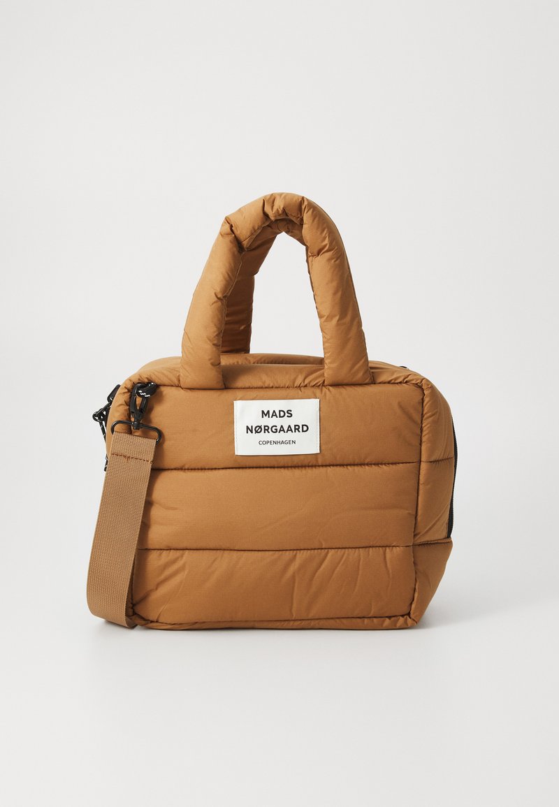 Sac en tissu matelassé brun avec des textures rembourrées, des poignées courtes, une bandoulière amovible et une étiquette blanche sur le devant.