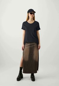 T-shirt nera, gonna di jeans marrone fino al ginocchio con spacco laterale, abbinata a stivali neri con plateau e un berretto nero. Tessuto liscio e vestibilità casual.