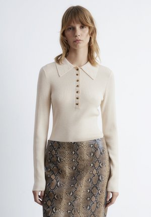 Knit cream sweater with ribbed texture, large collar, and buttoned front. Worn with a snakeskin-patterned brown skirt featuring darker accents.
