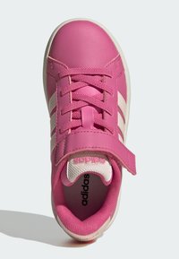 Růžová syntetická teniska s bílými prvky, kulatou špičkou, zavazováním na tkaničky a nastavitelným páskem. Texturovaný vnitřek a značkový jazyk.