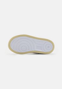 Weiße Sneaker-Sohle mit einer strukturierten GummOberfläche, konzentrischen kreisförmigen Mustern und einem hellbraunen Rand. Mit Nike-Logo gekennzeichnet.