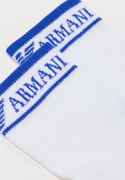 Λευκές κάλτσες crew με μπλε ριγέ μανσέτες, με υφασμένο το κείμενο "ARMANI" και το λογότυπο σε μπλε στο πάνω μέρος.