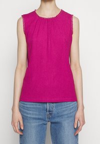 Fuchsia sleeveless top with textured fabric, gathered neckline, and decorative stitching along the collar and armholes. Paired with denim jeans.