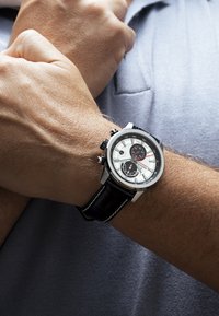 Chronograph-Uhr mit einem Silber- und Weißzifferblatt, schwarz-silbernem Metallgehäuse, schwarzem Lederarmband und mehreren Ziffernblättern zur Zeiterfassung.