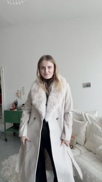 Μπεζ παλτό από μείγμα μαλλιού με ψεύτικη γούνινη κολαούζα, διπλής όψης σχέδιο, με δακτυλιοειδείς πέτο και πλαϊνές τσέπες. Απαλή υφή, μήκος μέχρι το μεσαίο μηρό.