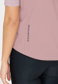 Helles rosa Sportshirt mit kurzen Ärmeln, das den Text "ENDURANCE" in Schwarz an der Seite zeigt; kombiniert mit schwarzen, figurbetonten Leggings.