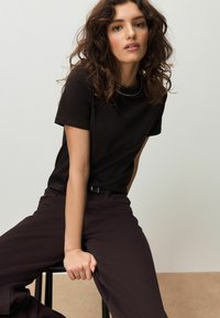 Crna majica kratkih rukava s okruglim izrezom, uparena s tamnim hlačama. Meka tekstura, kroj koji pristaje tijelu, minimalistički izgled i bez vidljivih uzoraka.