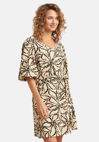 Beige jurk met zwarte bloemenprint, V-hals en korte pofmouwen, met een tailleband voor een verstelbare pasvorm. Zachte, gladde stof.