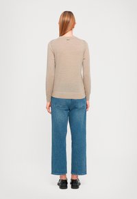Beiger Pullover mit rundem Halsausschnitt und langen Ärmeln, kombiniert mit blauen weit geschnittenen Jeans. Der Pullover hat eine glatte Textur und einen dezenten Glanz.