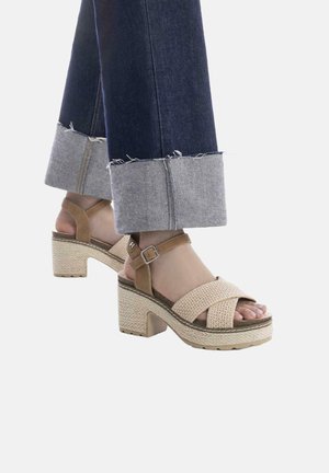 Sandali platform intrecciati beige con una cinghia alla caviglia marrone, un tacco a blocco testurizzato e una suola in gomma, abbinati a jeans di denim cropped.